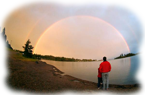 Hombre de rojo de pié, de espaldas frente a un lago y un arco iris